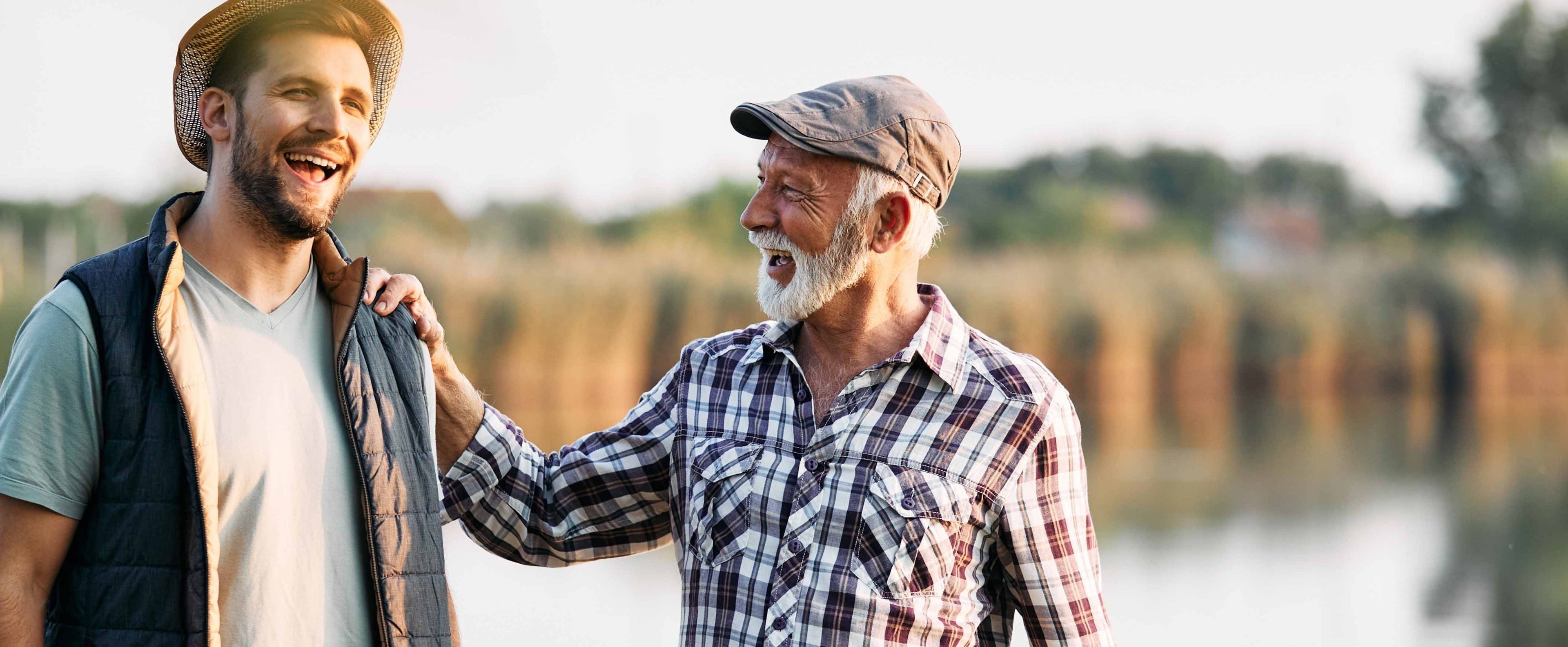 Two men standing by a lake with fishing rods, smiling and enjoying each other's company.